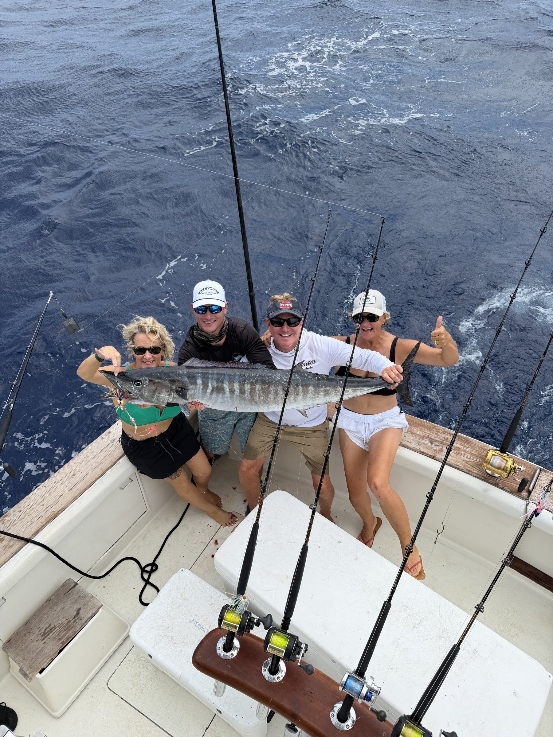 Four friends on deck holding a wahoo